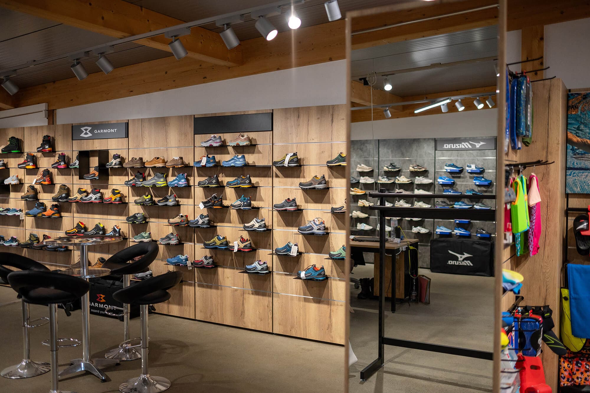 Catrade Aigles Showroom Schweiz Weiters Dekorspan,Wandanlage mit felxiblem Regalsystem. Dekorspan mit waremer Eiche H1180. Spiegelflächen. Schuhpräsentation. Warenträger aus Metall. Logotafel einhängbar