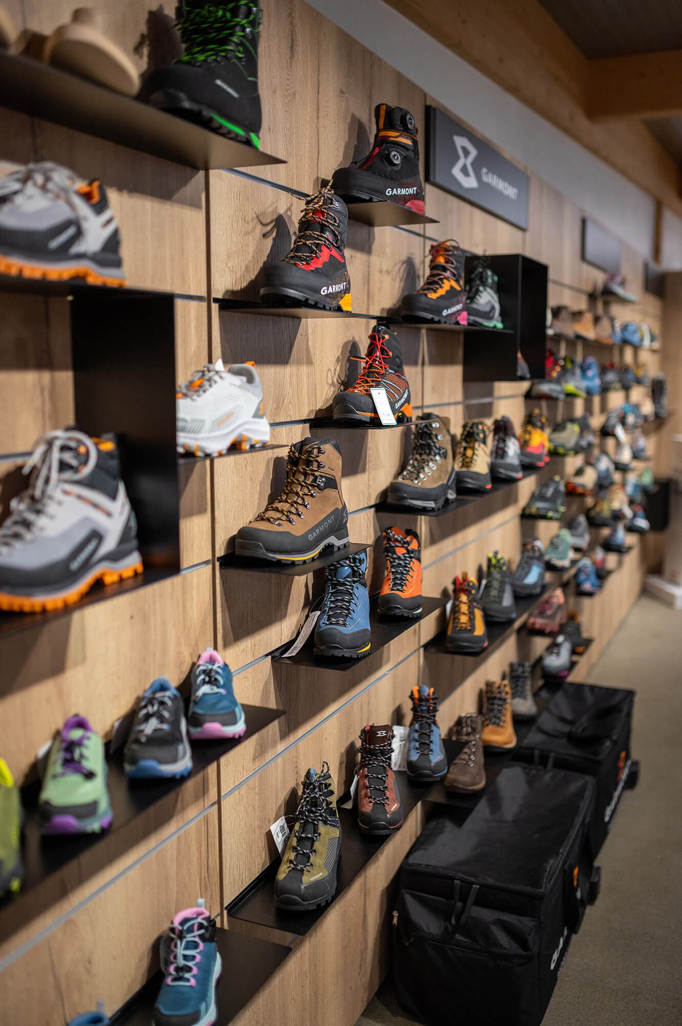 Catrade Aigles Showroom Schweiz Weiters Dekorspan, Detailfoto Schuhpräsentation, Lamellensystem, Tablare für Schuhe. Warenträger aus dunklem Metall und Wandanlage mit waremer Eiche Dekorspan H1180. Logotafeln aus Metall. felxibles Regalsystem.