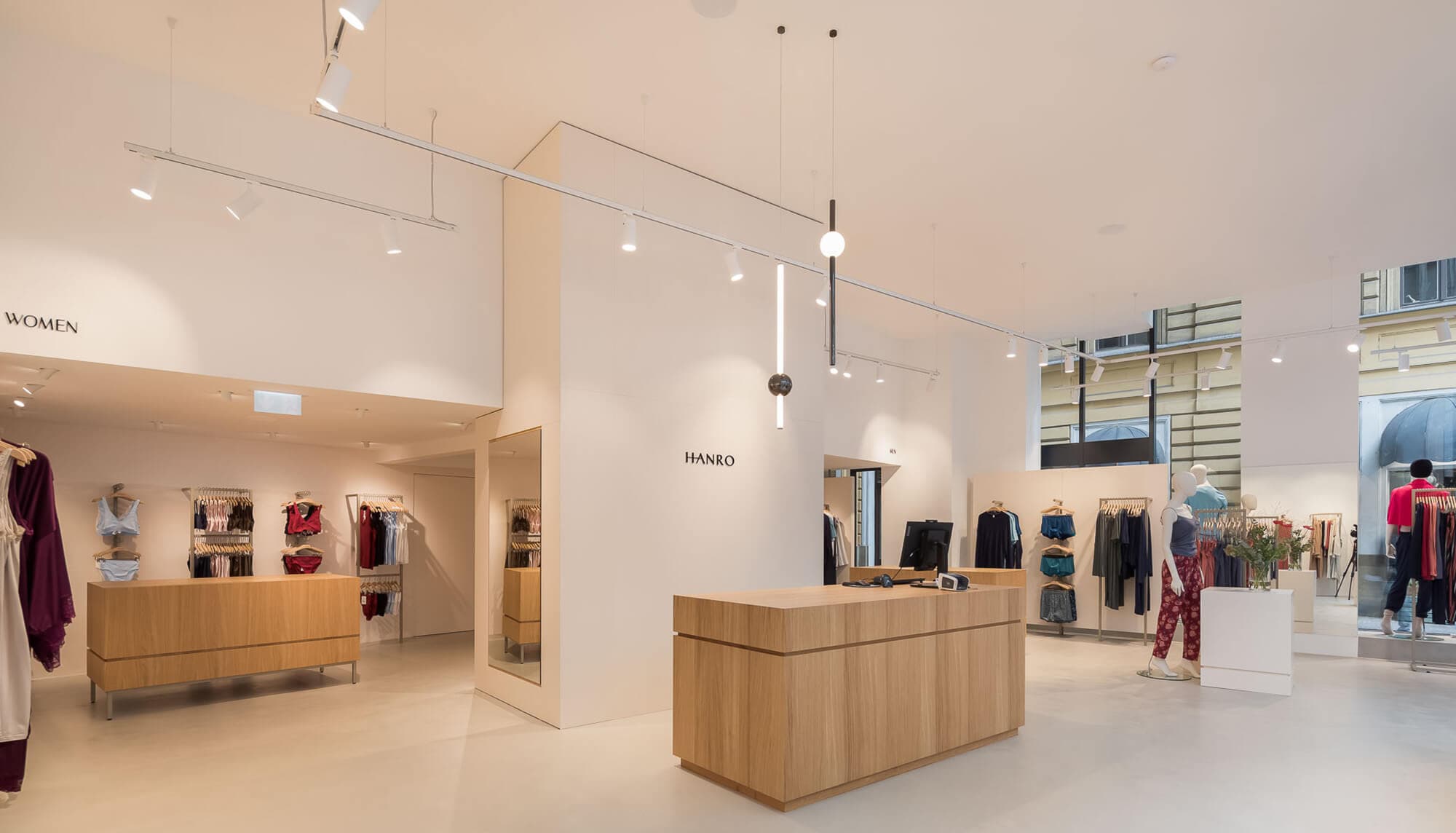 Hanro Tuchlauben, Wäsche, hocher heller Raum mit Kassatheke und Säulenverbau in Schleiflack. Warenpräsentation mit Gestänge an der Wand. Kassa in Eiche funiert natur lackiert